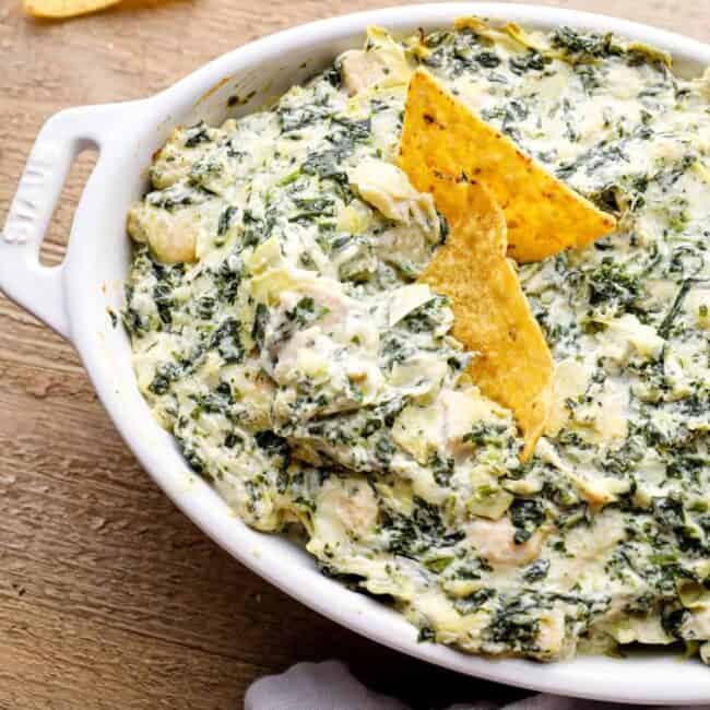 chicken spinach artichoke dip in a white baking dish with tortilla chips