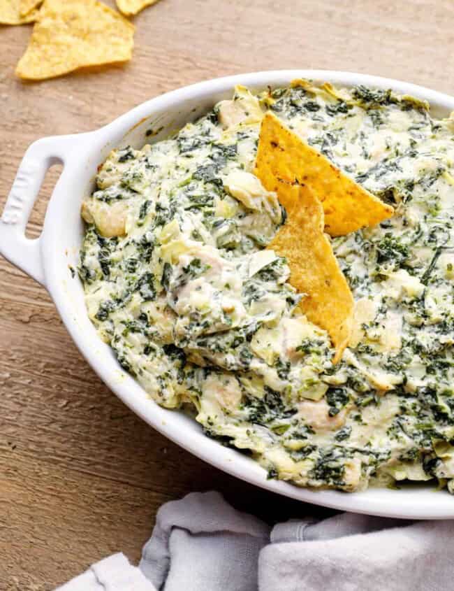 chicken spinach artichoke dip in a white baking dish with tortilla chips