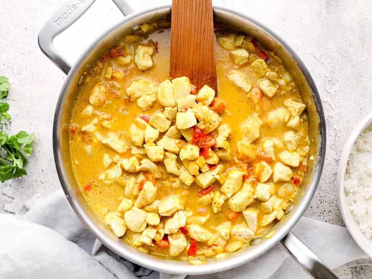 coconut curry chicken in a saucepan with a wood spoon