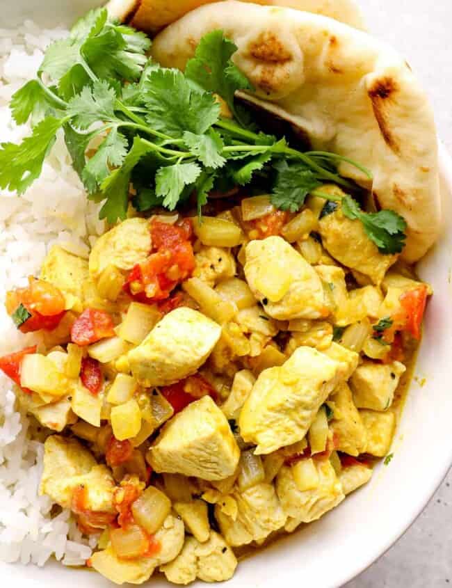 coconut curry chicken in a white bowl with rice and pita