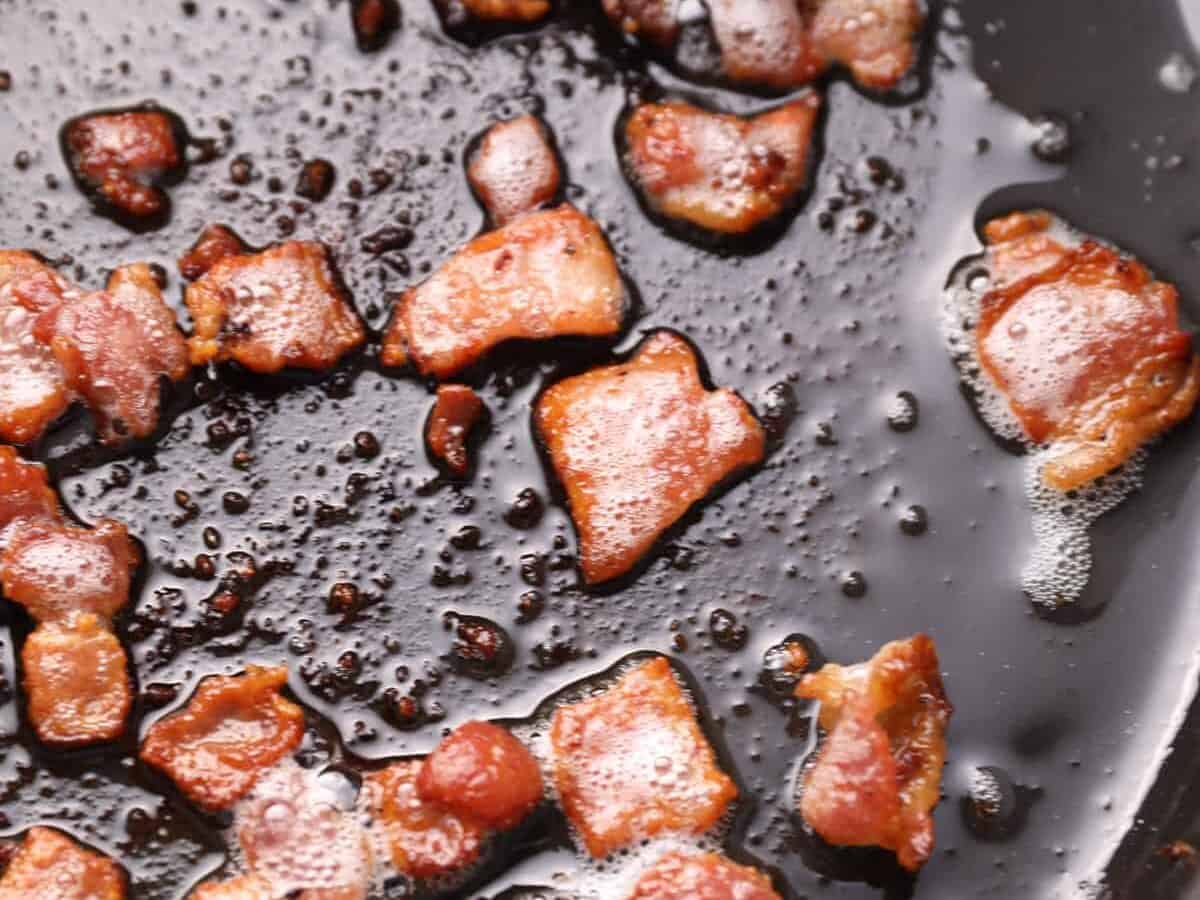 Pieces of bacon cooking in a skillet.