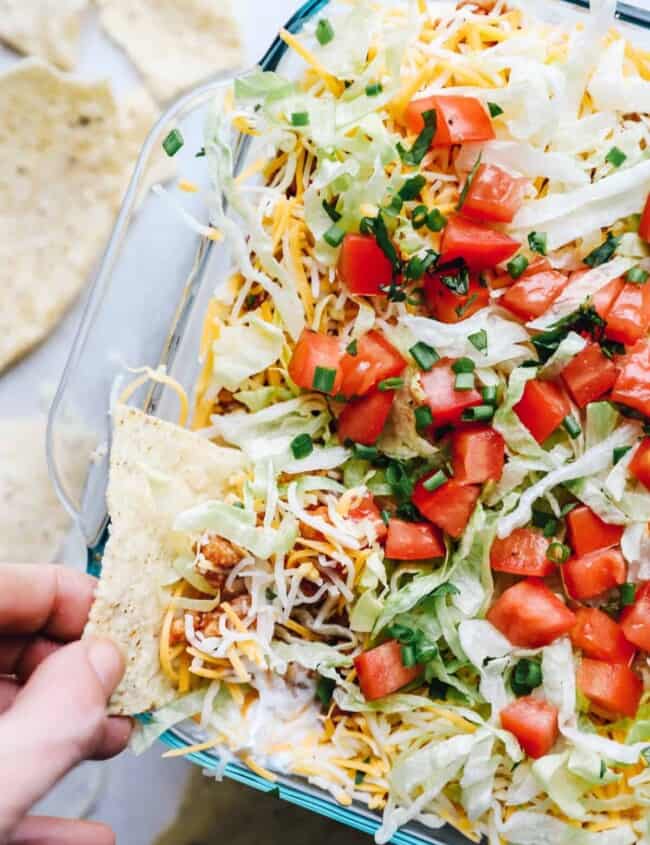 hand dipping a chip into layered chicken taco dip