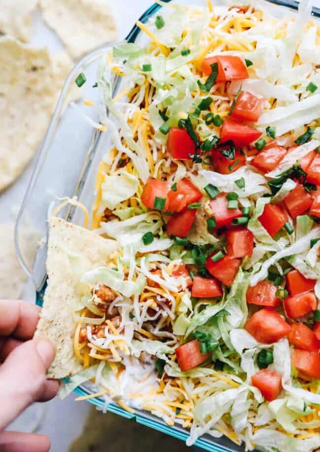 hand dipping a chip into layered chicken taco dip