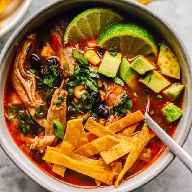 a bowl of authentic chicken tortilla soup, with chicken, tortilla strips, limes, avocado, and more
