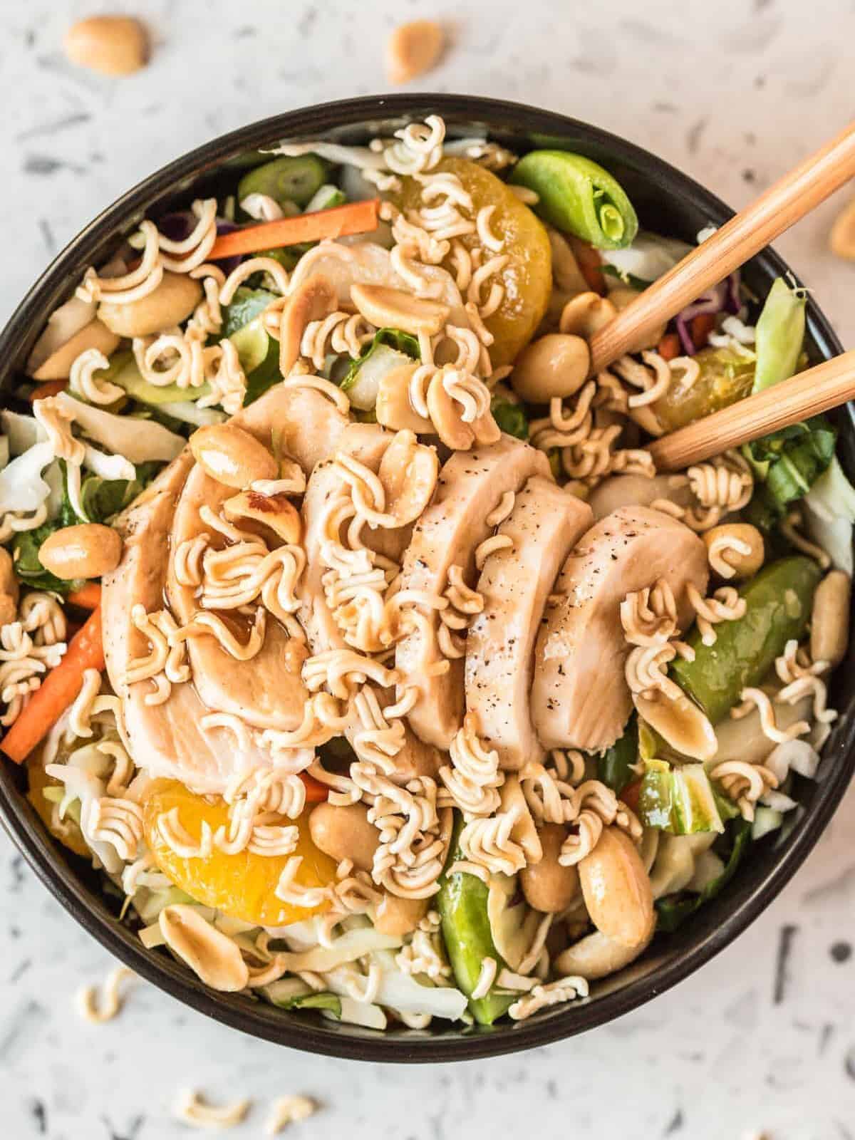 A bowl of Chinese chicken salad with ramen noodles, chopped chicken, peanuts, dressing, mandarin oranges, and veggies.