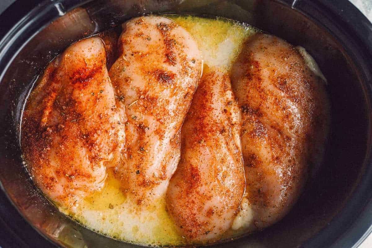 Seasoned chicken breasts in a slow cooker with liquid.