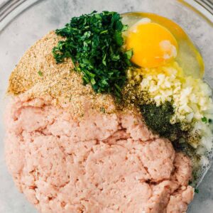 Ingredients for Greek chicken meatballs in glass mixing bowl