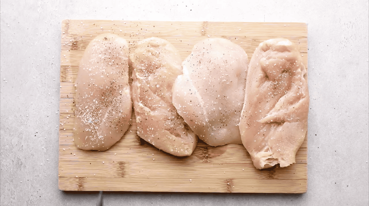 Raw seasoned chicken breasts on a cutting board.