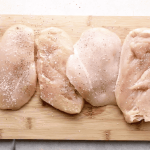 Raw seasoned chicken breasts on a cutting board.