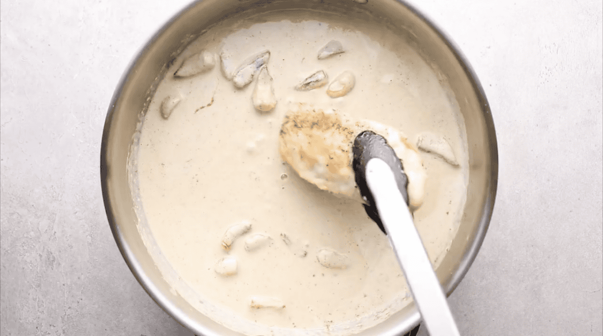 placing chicken breasts in a pan of garlic cream sauce.