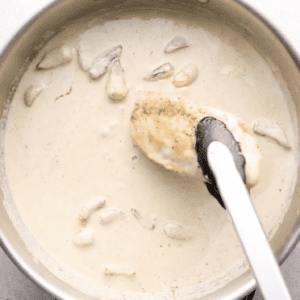 placing chicken breasts in a pan of garlic cream sauce.