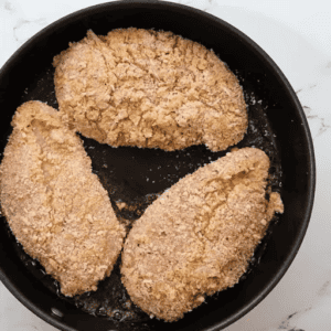 Three breaded chicken breasts in a skillet.