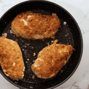 Three breaded chicken breasts browning in a skillet for crockpot chicken parmesan.