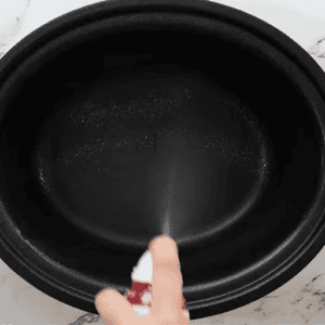 A crockpot being sprayed with cooking spray.