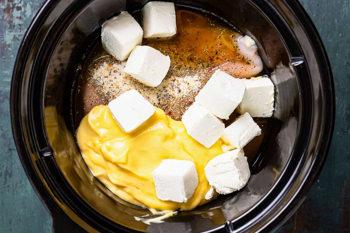 Chicken, cubes of cream cheese, broth, and cream of chicken soup in a crock pot.