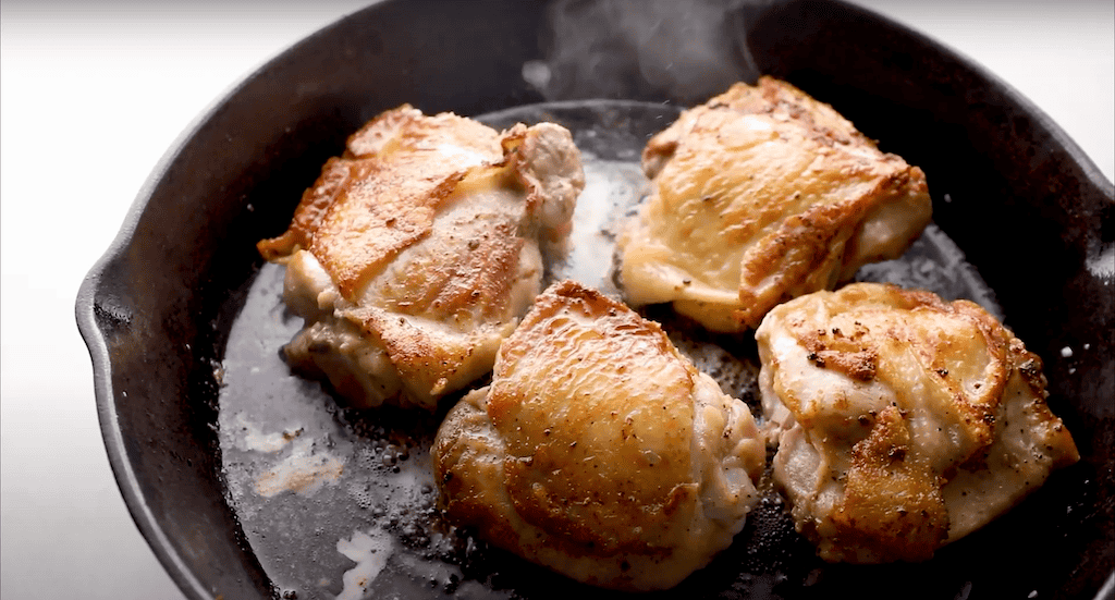 Chicken thighs browning in a skillet.