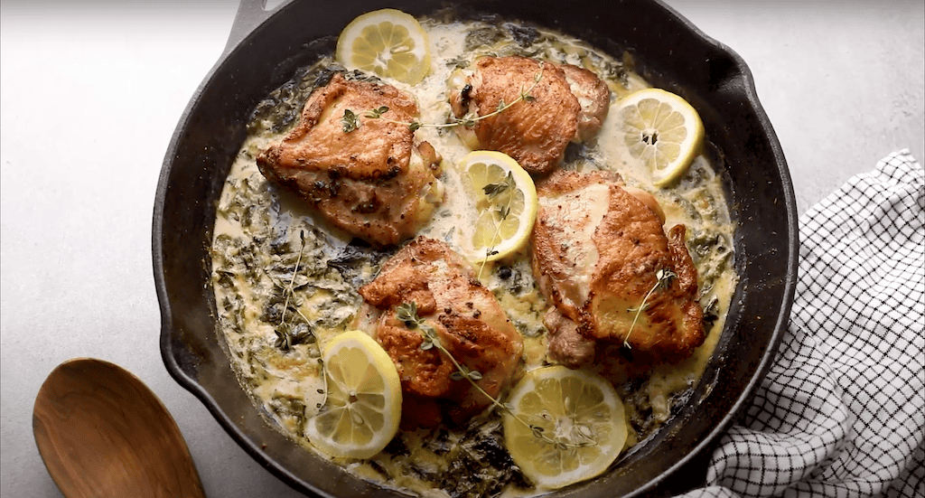 Chicken thighs in a creamy lemon butter sauce with spinach and lemon slices; in a cast iron skillet.