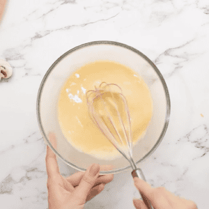 Whisking eggs and milk in a glass mixing bowl.