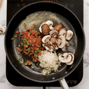 Diced onions, sliced mushrooms, and diced peppers in a skillet.