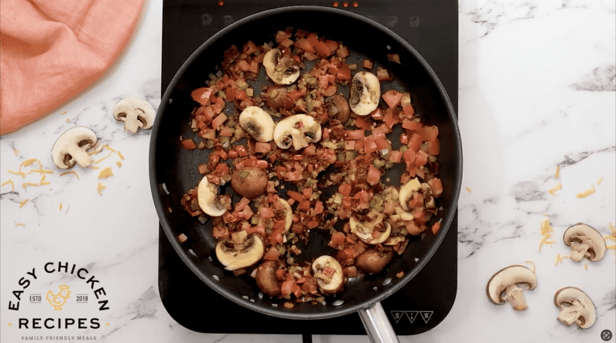 Tomatoes, bacon, mushrooms, and peppers cooking in a skillet.