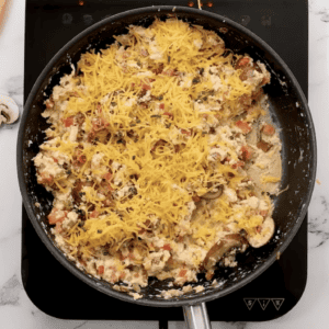 Loaded scrambled eggs in a skillet, topped with shredded cheese.