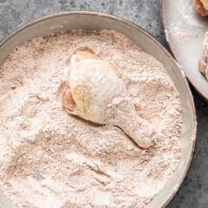Raw chicken drumstick in a bowl of seasoned flour.
