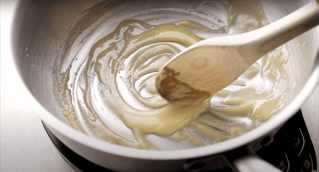 A wooden spoon stirring together butter and flour in a pan.