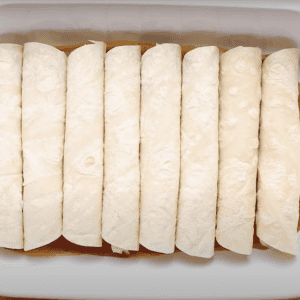 8 rolled enchiladas lined up in a casserole dish.