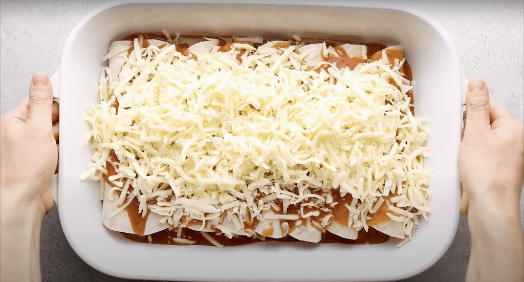 Enchiladas topped with sauce and shredded cheese before being baked.
