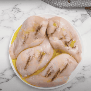 4 raw chicken breasts on a plate, covered in olive oil, salt and pepper.