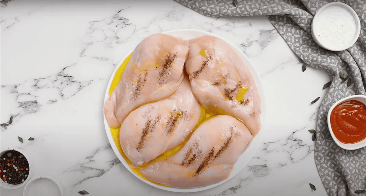 4 raw chicken breasts on a plate, covered in olive oil, salt and pepper.