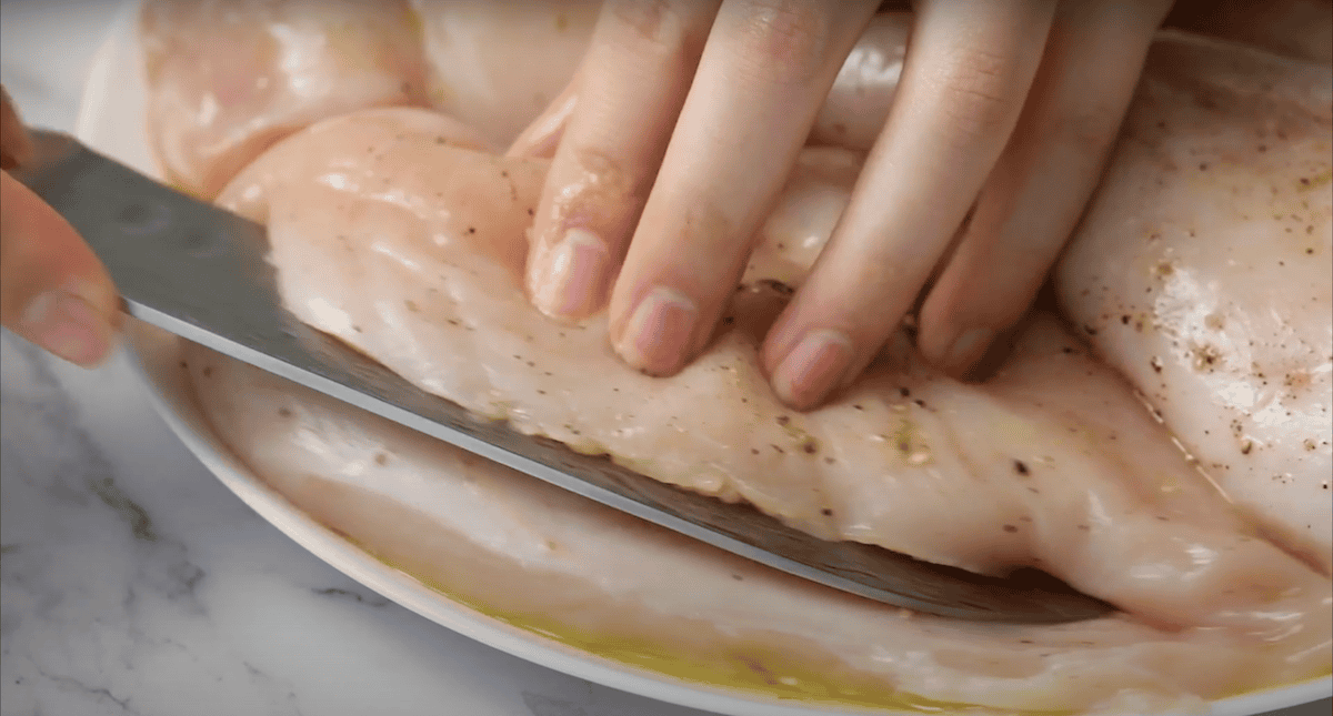 Knife cutting a pocket into the side of a chicken breast.