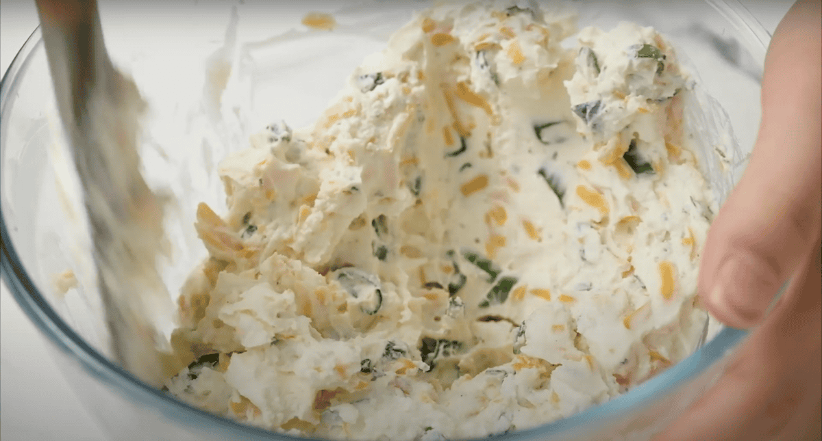 Combining cream cheese, shredded cheese, and green onions in a glass mixing bowl.