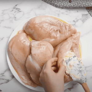 Hand using a rubber spatula to stuff a cream cheese mixture into uncooked chicken breasts.