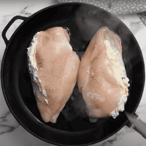 2 stuffed chicken breasts searing in a skillet.