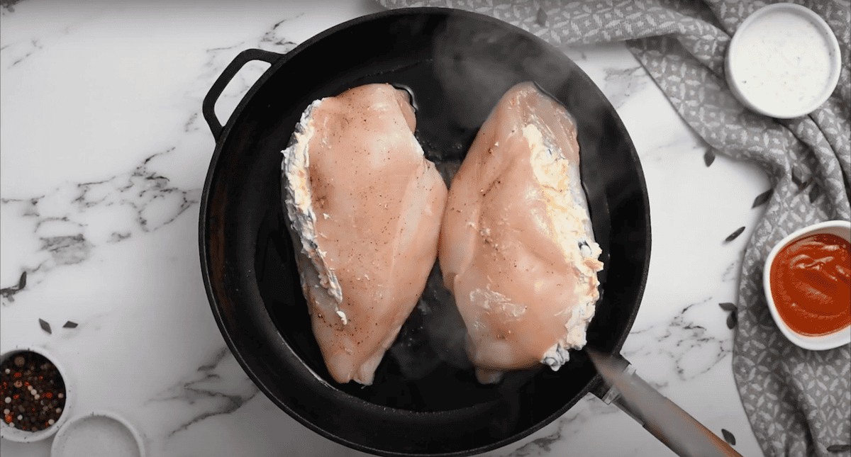 2 stuffed chicken breasts searing in a skillet.