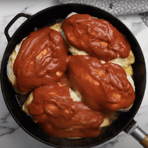 4 stuffed chicken breasts in a skillet, covered in buffalo sauce.