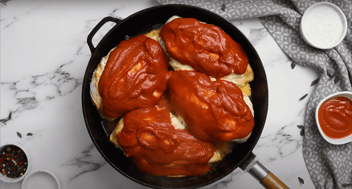 4 stuffed chicken breasts in a skillet, covered in buffalo sauce.