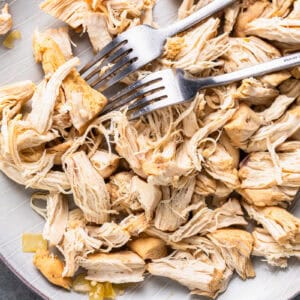 Pieces of shredded chicken on a plate with two forks.