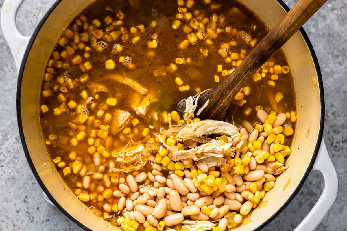 Corn, white beans, chicken, and broth combined in a large pot.
