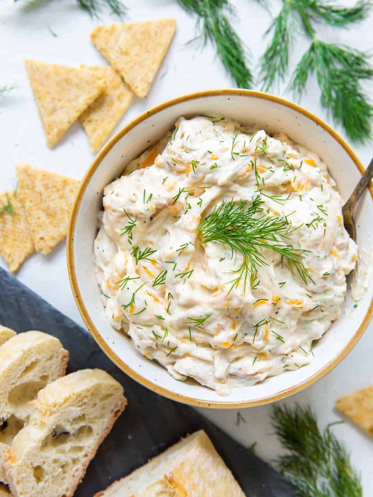 overhead view of a bowl of ranch chicken dip with crackers and pieces of bread surrounding it.