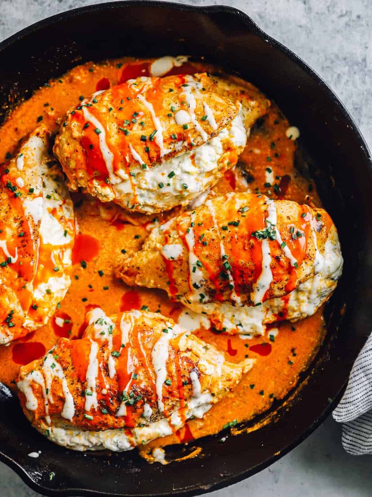 4 buffalo stuffed chicken breasts in a skillet, covered with ranch.