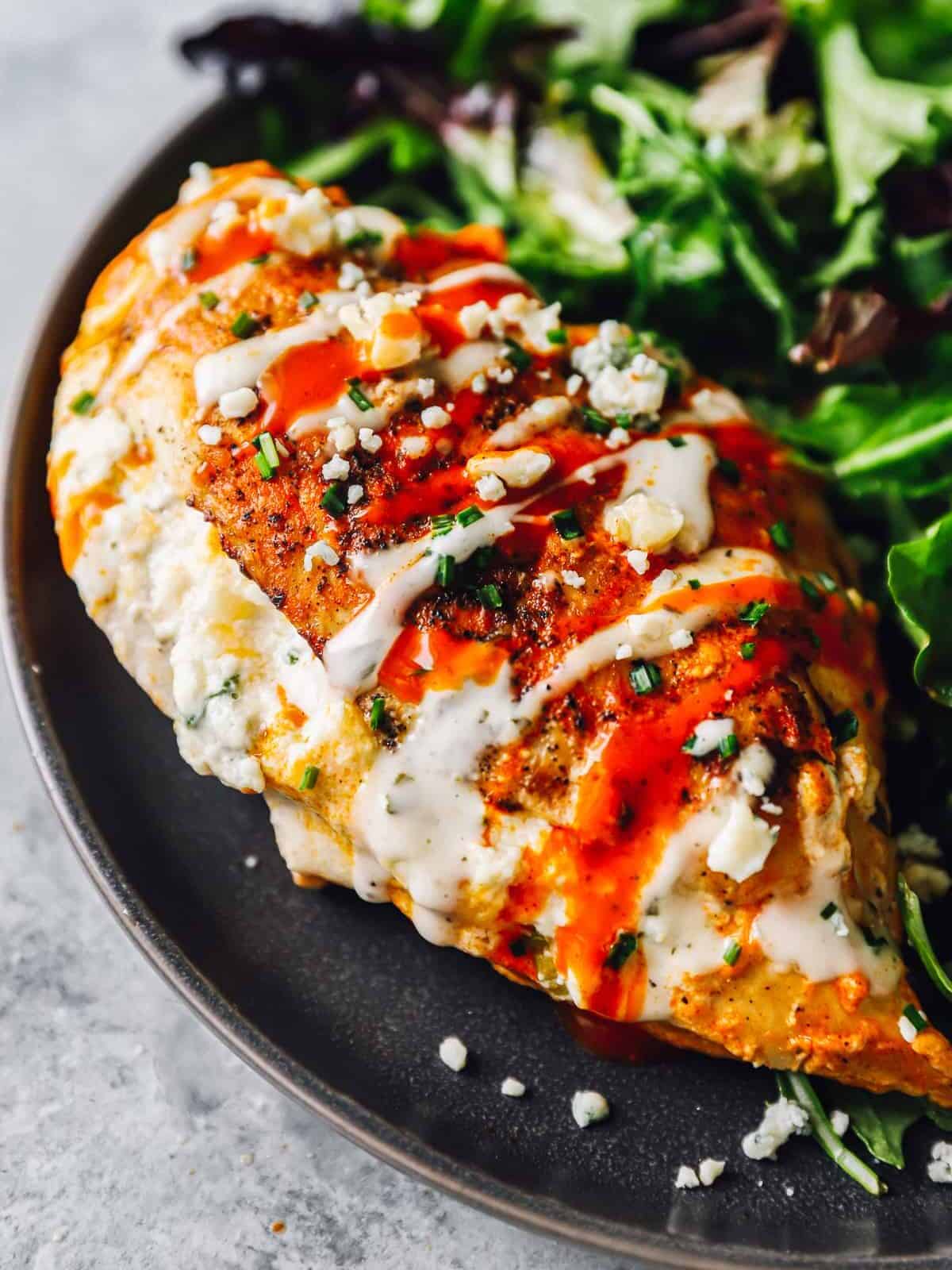 stuffed buffalo chicken breast on a black plate with salad.