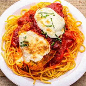 stuffed chicken parmesan over pasta on a white plate.