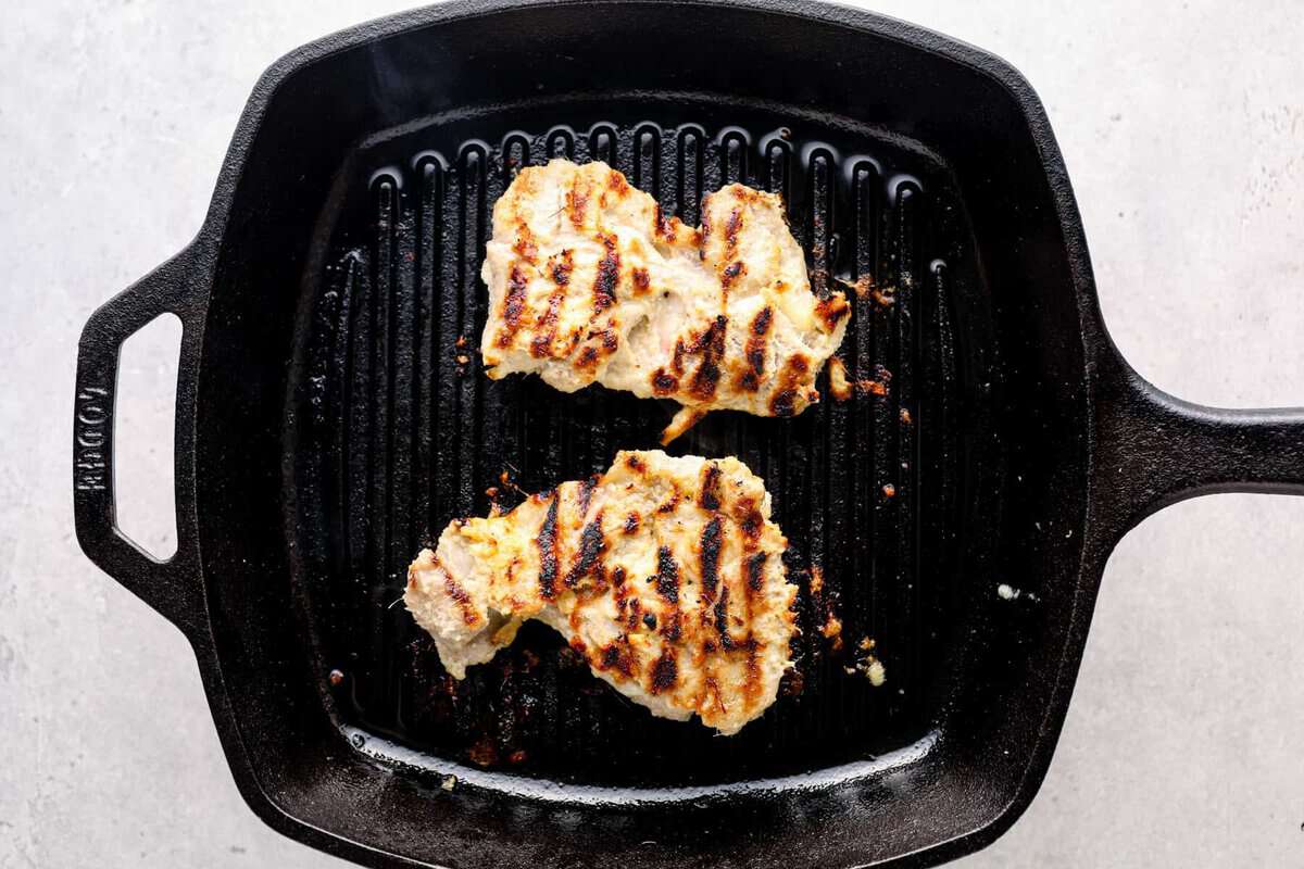 Marinated chicken thighs cooking on a grill pan.