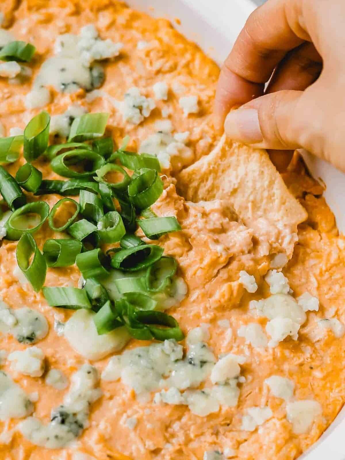 A chip scooping up some buffalo chicken dip topped with blue cheese crumbles and green onions.