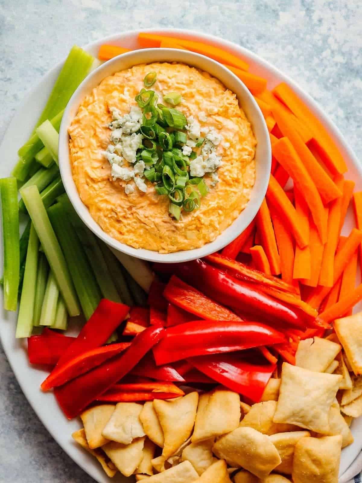 A serving platter filled with veggie sticks, and a bowl of buffalo chicken dip.