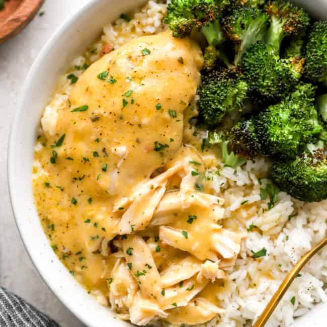 a serving of shredded crockpot ranch chicken in a white bowl with rice and broccoli.