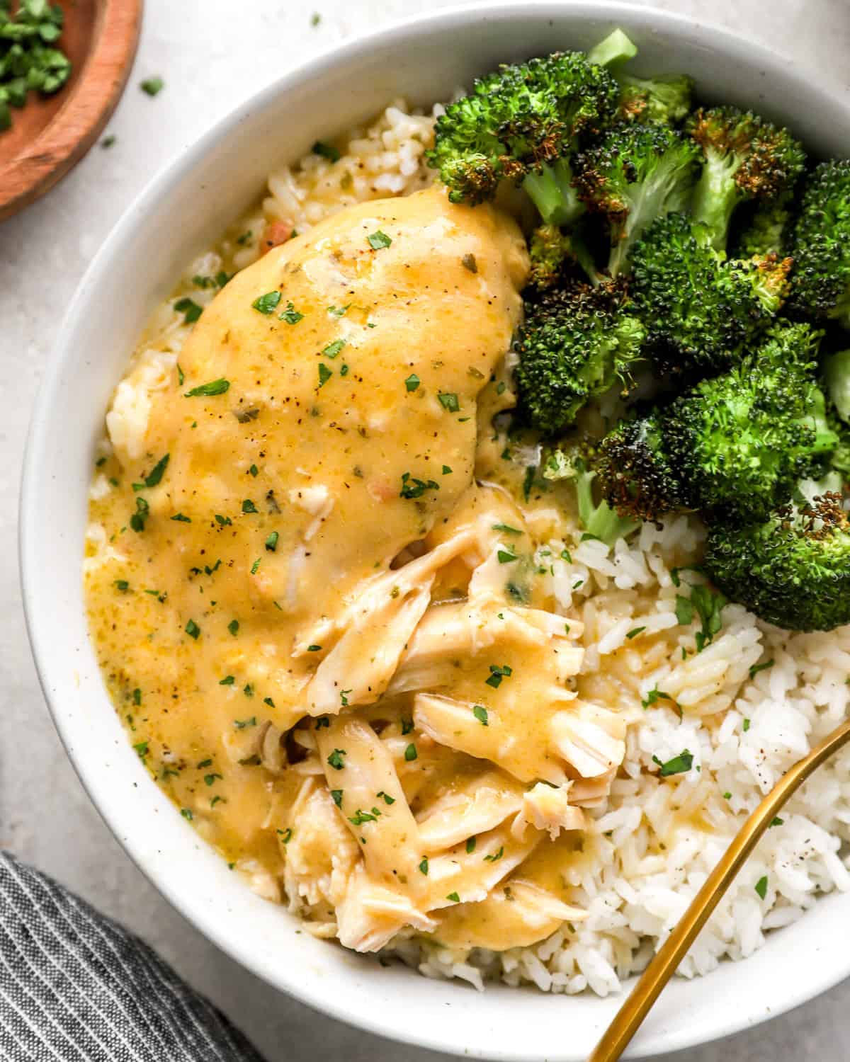 a serving of shredded creamy ranch chicken in a white bowl with rice and broccoli.