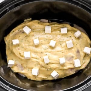 raw chicken breasts topped with ranch sauce and cubes of cream cheese in a crockpot.